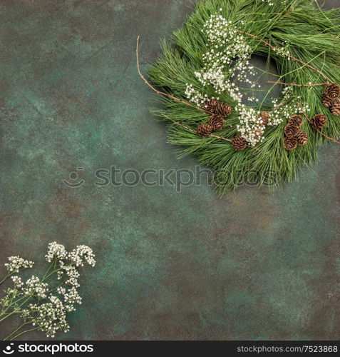 Christmas wreath with pine cones and white flowers on stone background. Festive arrangement