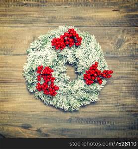 Christmas wreath with red berries over wooden background. Festive decoration. Vintage style toned picture