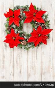 Christmas wreath with red poinsettia flowers on bright wooden background. Christmas decoration