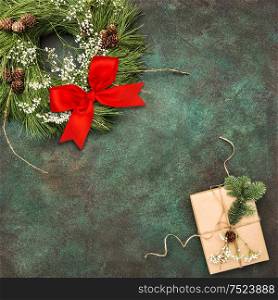 Christmas wreath with red ribbon bow and wrapped gift on stone background. Festive arrangement