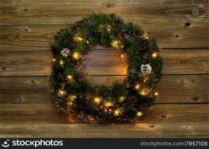 Christmas wreath with white lights on rustic wooden boards. Low lighting to bring out glow of lights.