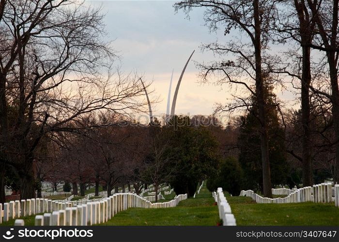 Christmas wreaths on gravestones in Arlington National Cemetery. Air Force memorial soars in the distance as the sun sets at dusk