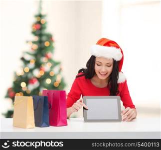 christmas, x-mas, electronics, gadget concept - smiling woman in santa helper hat with blank screen tablet pc and shopping bags