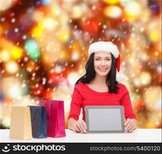 christmas, x-mas, electronics, gadget concept - smiling woman in santa helper hat with blank screen tablet pc and shopping bags