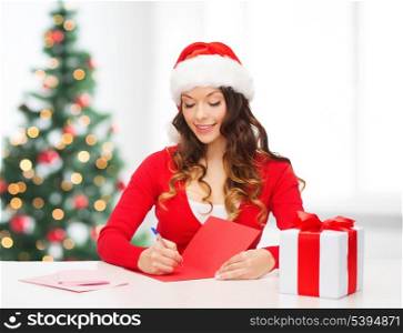 christmas, x-mas, gifts, presents, celebration concept - smiling woman in santa helper hat with gift box and postcard