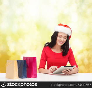 christmas, x-mas, online shopping and electronics concept - smiling woman in santa helper hat with shopping bags and tablet pc computer