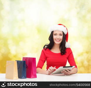 christmas, x-mas, online shopping and electronics concept - smiling woman in santa helper hat with shopping bags and tablet pc computer