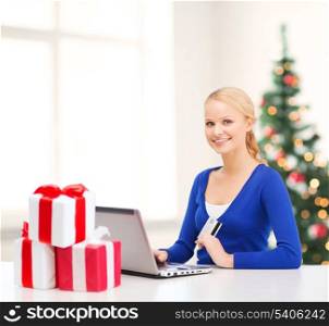 christmas, x-mas, online shopping concept - smiling woman with gift boxes, laptop computer and credit card