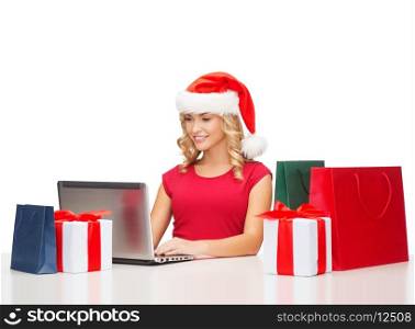 christmas, x-mas, online shopping concept - woman in santa helper hat with gift boxes, bags and laptop computer