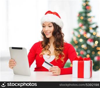 christmas, x-mas, online shopping concept - woman in santa helper hat with gift box, tablet pc computer and credit card