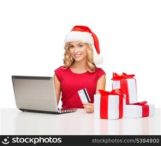 christmas, x-mas, online shopping concept - woman in santa helper hat with gift boxes, laptop computer and credit card