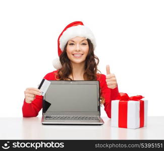 christmas, x-mas, online shopping concept - woman in santa helper hat with gift box, laptop computer and credit card