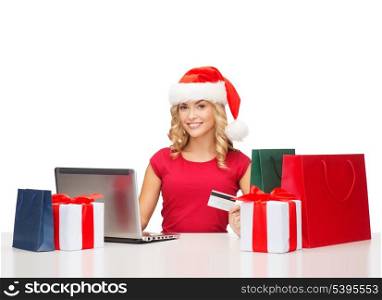 christmas, x-mas, online shopping concept - woman in santa helper hat with gift boxes, bags, laptop computer and credit card