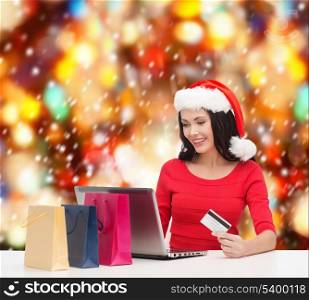 christmas, x-mas, online shopping concept - woman in santa helper hat with shoopping bags, laptop computer and credit card