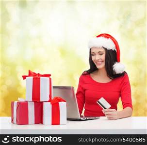 christmas, x-mas, online shopping concept - woman in santa helper hat with gift boxes, laptop computer and credit card