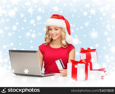 christmas, x-mas, online shopping concept - woman in santa helper hat with gift boxes, laptop computer and credit card