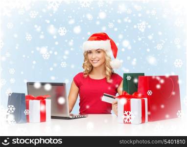 christmas, x-mas, online shopping concept - woman in santa helper hat with gift boxes, bags, laptop computer and credit card