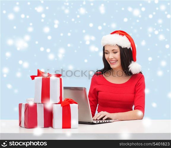 christmas, x-mas, online shopping concept - woman in santa helper hat with gift boxes and laptop computer