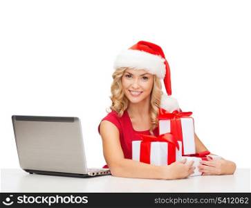 christmas, x-mas, online shopping concept - woman in santa helper hat with gift boxes and laptop computer