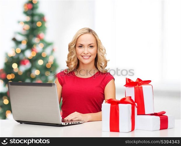 christmas, x-mas, online shopping concept - woman with gift boxes and laptop computer