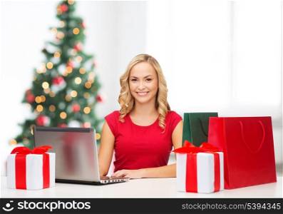 christmas, x-mas, online shopping concept - woman with gift boxes, bags and laptop computer