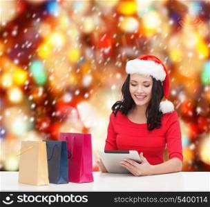 christmas, x-mas, online shopping, electronics concept - smiling woman in santa helper hat with shopping bags and tablet pc computer