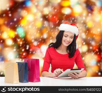 christmas, x-mas, online shopping, electronics concept - smiling woman in santa helper hat with shopping bags and tablet pc computer