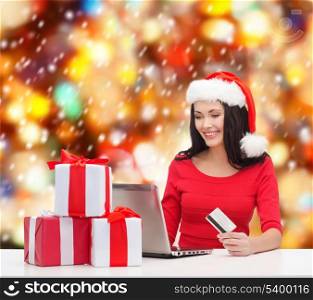 christmas, x-mas, online shopping, electronics concept - woman in santa helper hat with gift boxes, laptop computer and credit card