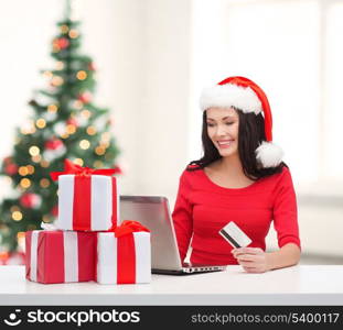 christmas, x-mas, online shopping, electronics concept - woman in santa helper hat with gift boxes, laptop computer and credit card