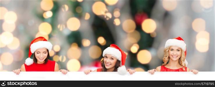 christmas, x-mas, people, advertisement and sale concept - happy women in santa helper hat with blank white board over tree lights background