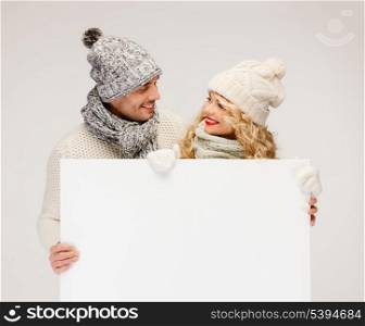 christmas, x-mas, people, advertisement, couple, sale concept - happy woman and man in winter clothes with blank white board
