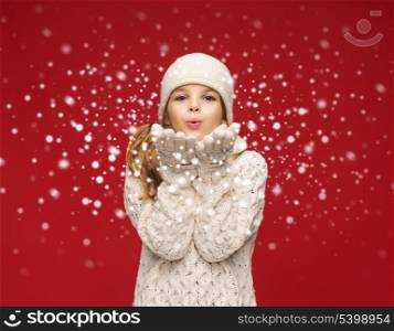 christmas, x-mas, people, happiness concept - happy girl in winter clothes blowing on palms