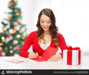 christmas, x-mas, valentine&#39;s day, celebration concept - smiling woman in red clothes with gift box and postcard