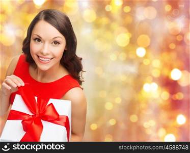christmas, x-mas, valentines day, people and celebration concept - smiling woman in red dress with gift box over holidays lights background