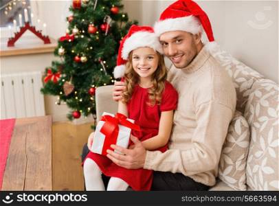 christmas, x-mas, winter, happiness and people concept - smiling father and daughter in santa helper hats holding gift box