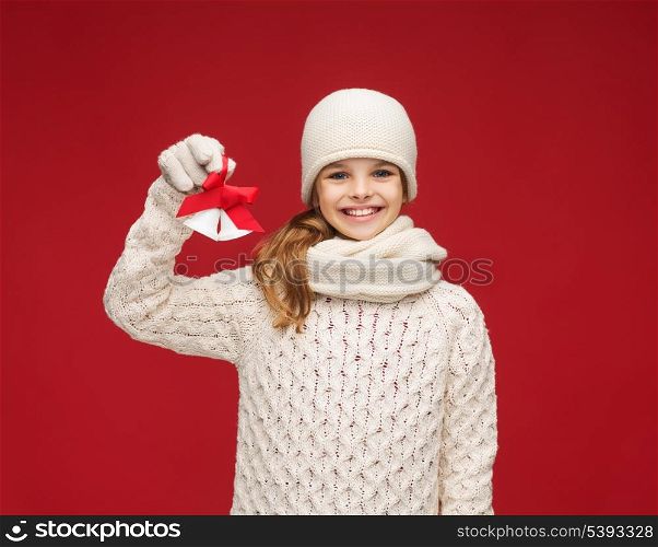 christmas, x-mas, winter, happiness concept - smiling girl in hat, muffler and gloves with jingle bells