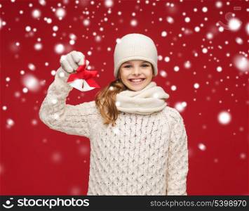 christmas, x-mas, winter, happiness concept - smiling girl in hat, muffler and gloves with jingle bells