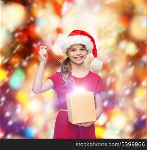 christmas, x-mas, winter, happiness concept - smiling girl in santa helper hat with gift box and magic wand