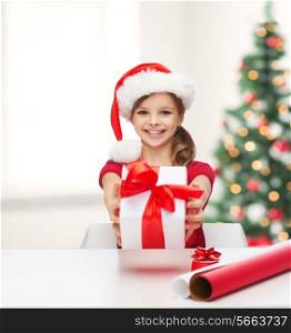 christmas, x-mas, winter, happiness concept - smiling girl in santa helper hat with gift box and wrapping paper