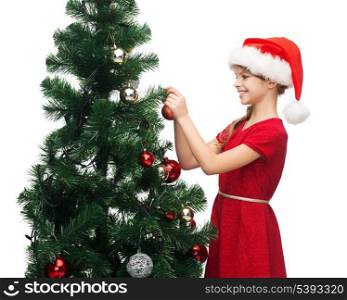 christmas, x-mas, winter, happiness concept - smiling girl in santa helper hat decorating a tree