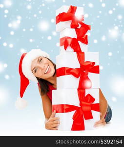 christmas, x-mas, winter, happiness concept - smiling woman in santa helper hat with many gift boxes