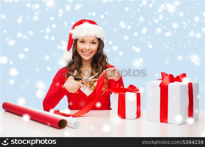 christmas, x-mas, winter, happiness concept - smiling woman in santa helper hat with gift box, wrapping paper and ribbon
