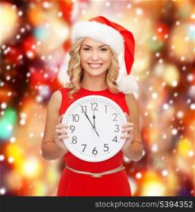 christmas, x-mas, winter, happiness concept - smiling woman in santa helper hat with clock showing 12