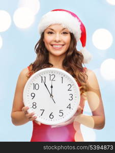 christmas, x-mas, winter, happiness concept - smiling woman in santa helper hat with clock showing 12