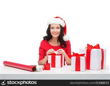 christmas, x-mas, winter, happiness concept - smiling woman in santa helper hat with many gift boxes and wrapping paper