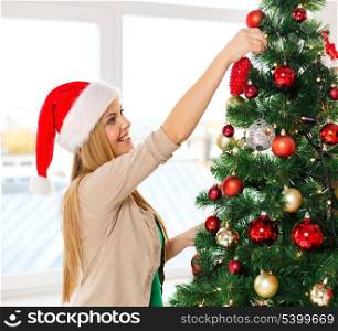 christmas, x-mas, winter, happiness concept - smiling woman in santa helper hat decorating a christmas tree