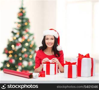 christmas, x-mas, winter, happiness concept - smiling woman in santa helper hat with many gift boxes and wrapping paper