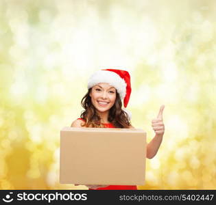 christmas, x-mas, winter, happiness concept - smiling woman in santa helper hat with parcel box showing thumbs up