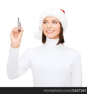 christmas, x-mas, winter, happiness concept - smiling woman in santa helper hat drawing or writing something in the air
