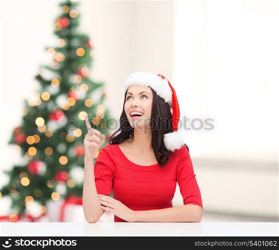 christmas, x-mas, winter, happiness concept - smiling woman in santa helper hat pointing to something
